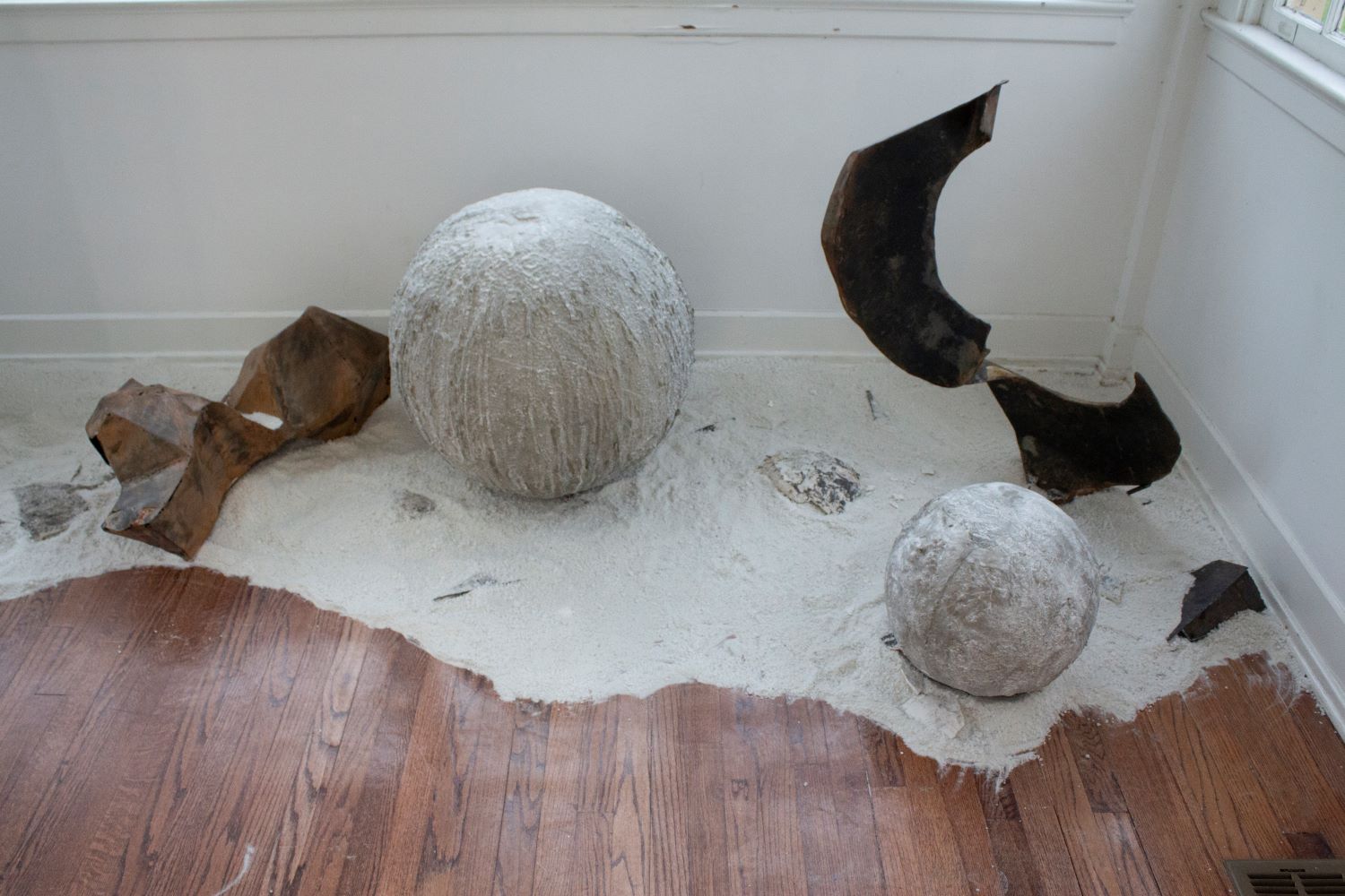 2 large concrete orbs with 2 large metal sculptures sitting in sand, similar to a landscape.