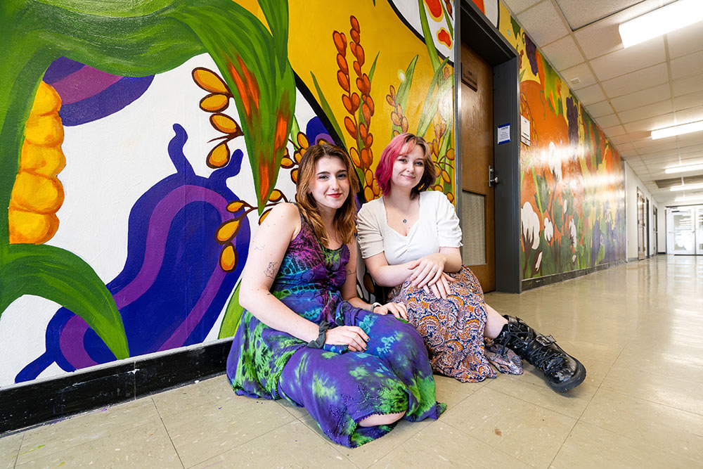 MSU art students Chloe V. Ruggiero, left, and Abbey R. Temple sit in front of the mural they painted on campus