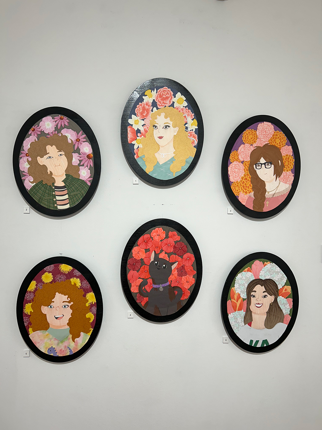 A collection of six cut-paper portraits. Each portrait is placed on a black plywood oval.