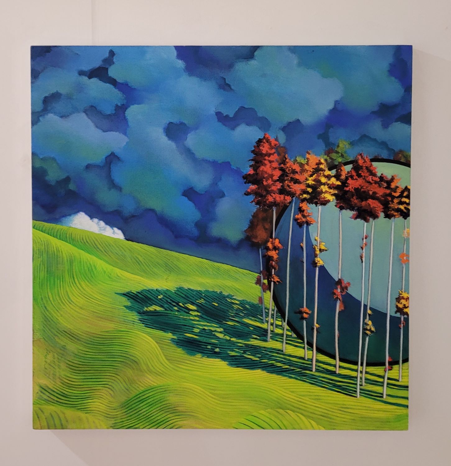 Large painting of a surreal landscape, has large 2D ball surrounded by trees, wavy grass, and abstract clouds. 