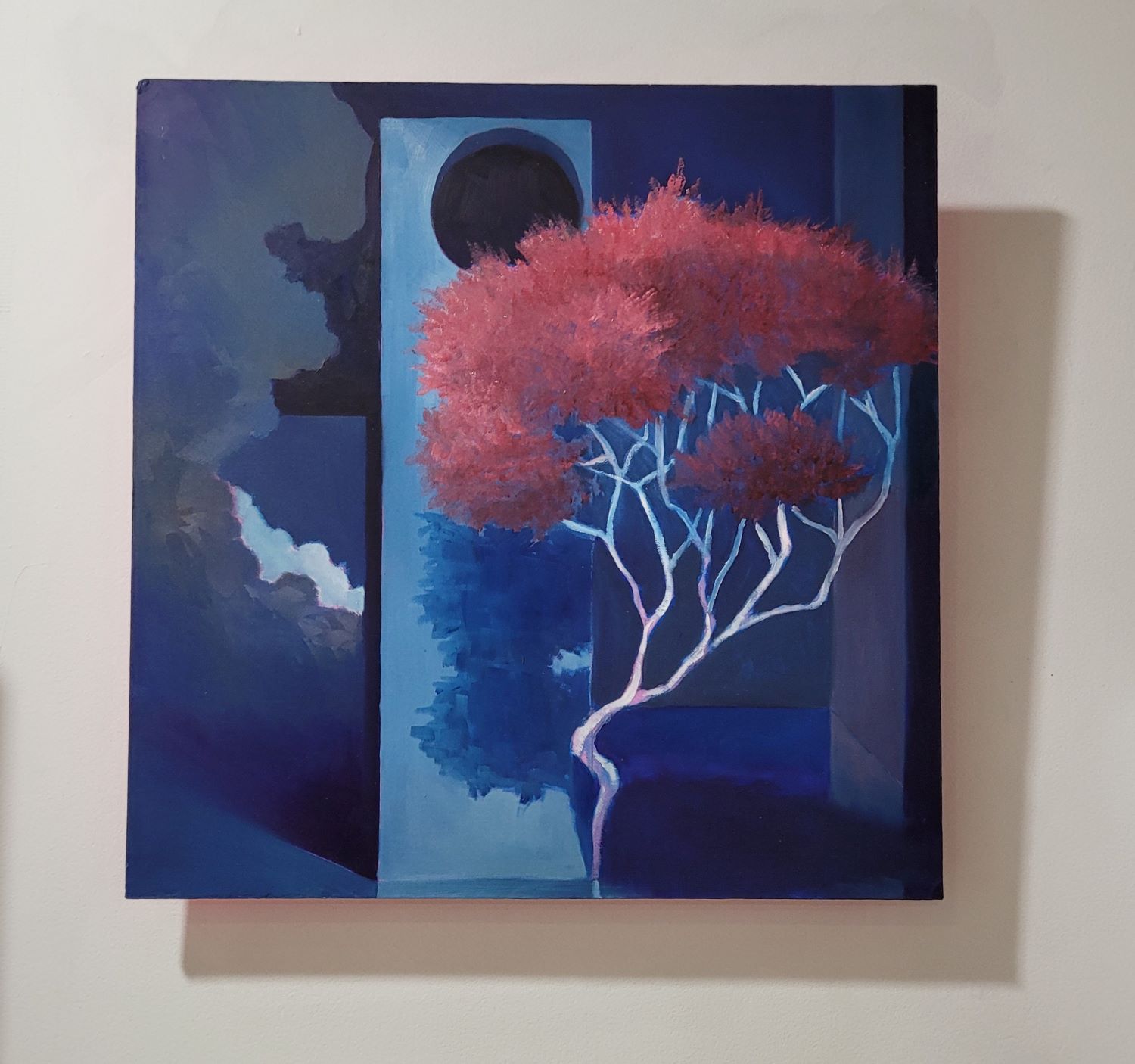 Small painting of a surreal, blue interior space with a large red tree and clouds in the middle of it. 